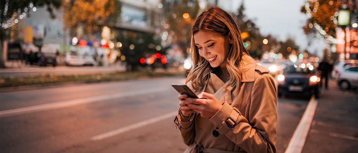 Woman looks at smartphone as evening falls on a metropolitan street.