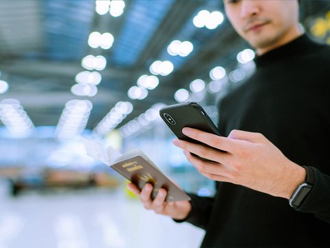 A man stands in an airport holding his smartphone in one hand and his passport in the other