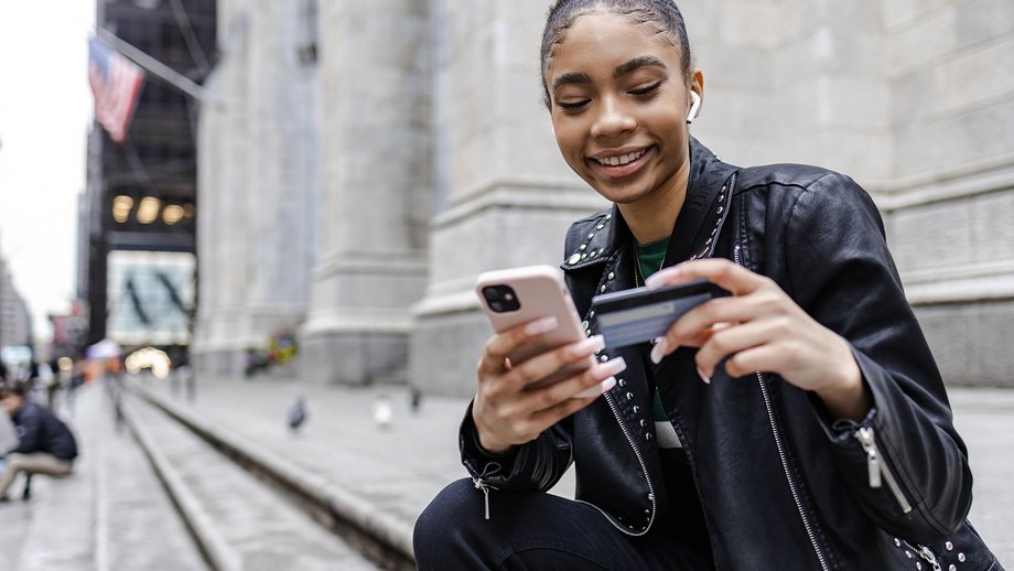 Young woman uses her smartphone and credit card sitting outside on the stairs.