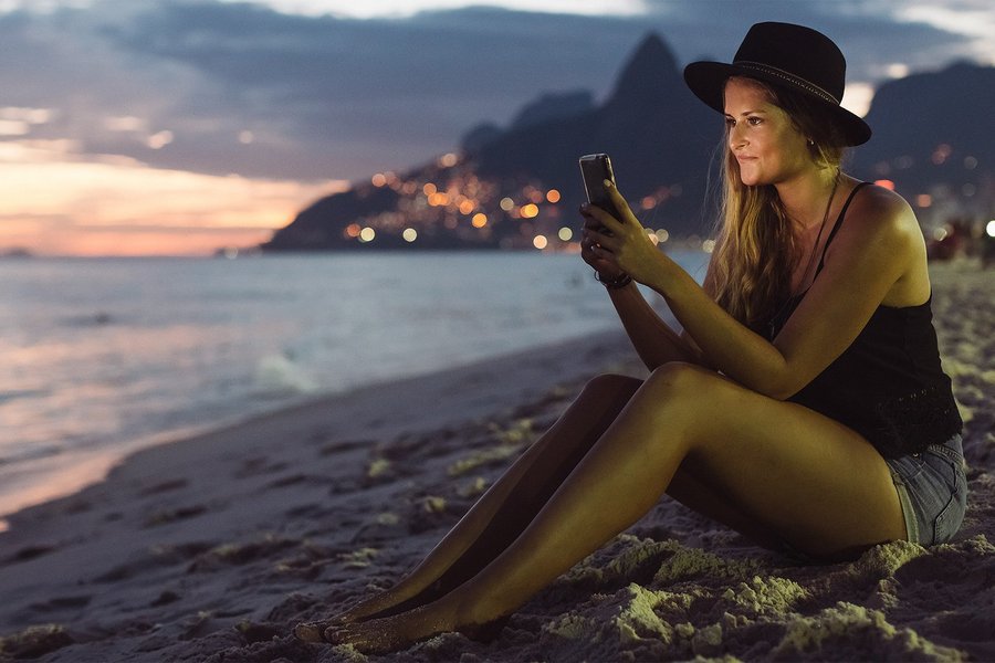 Young woman sitting at beach at night, looking at her mobile phone