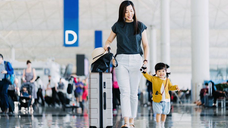 Eine fröhliche Mutter, die ihre Tochter an der Hand hält, geht durch die Flughafenhalle und reist mit dem Flugzeug in den Urlaub. 