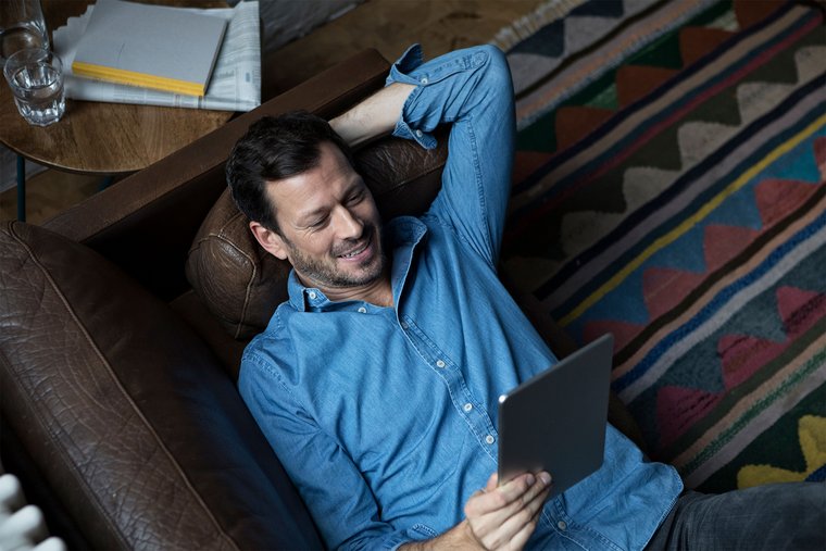 Man lying on his back smiling and having a tablet in his hand enjoying eGovernment