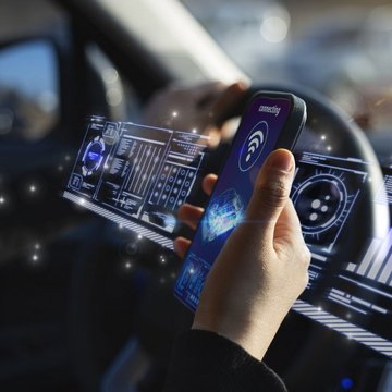 Hand holding smartphone in car with digital displays.