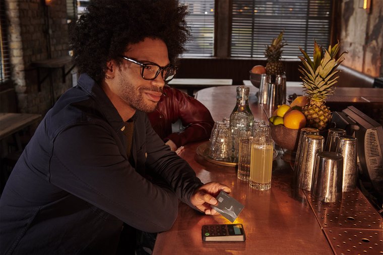 A smiling man sitting at a bar holding his credit card 