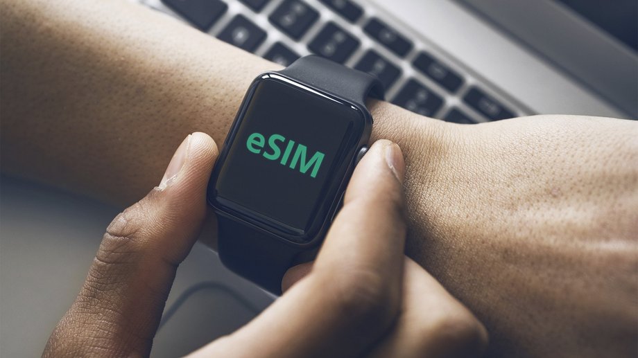 Focus on a smart watch displaying eSIM held by a woman in front of a computer.