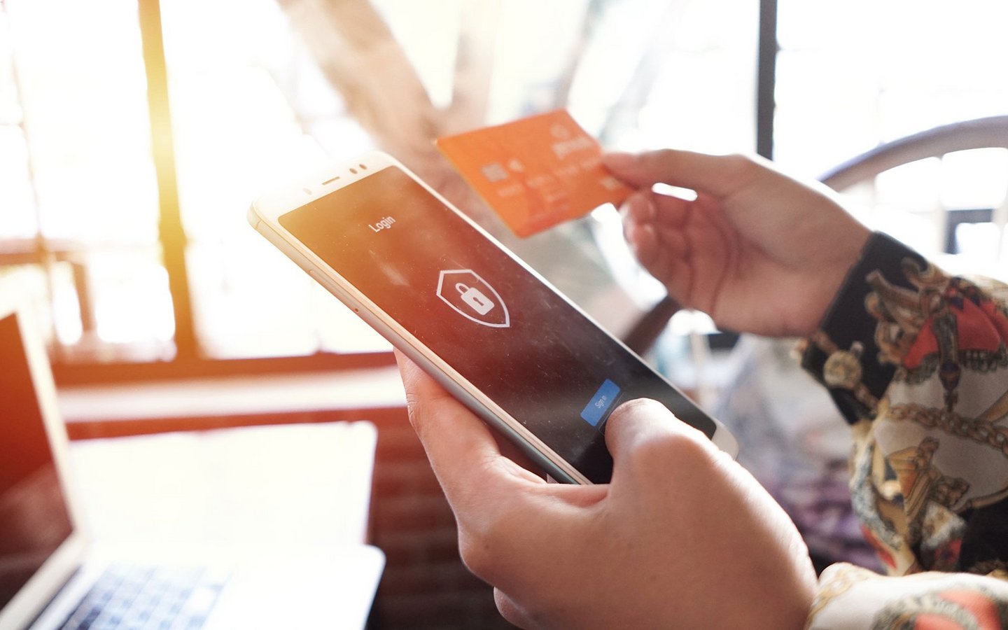 Die linke Hand hält ein Smartphone, das eine Zahlung auf einem Login-Bildschirm verifiziert, die rechte Hand hält eine Kreditkarte.