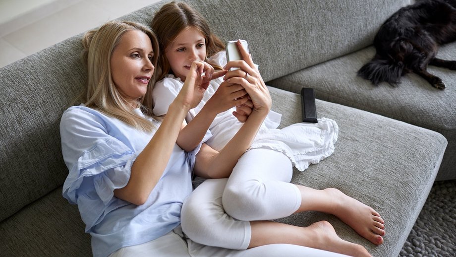 Mutter und Tochter auf dem Sofa mit einem Mobiltelefon, auf dem eine Smart Wallet geöffnet ist 