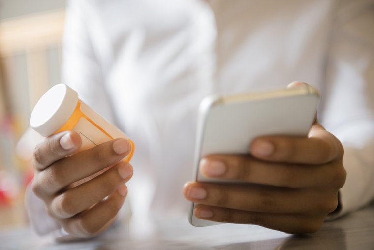 Man holding orange medical tablet container and mobile phone representing mobile health